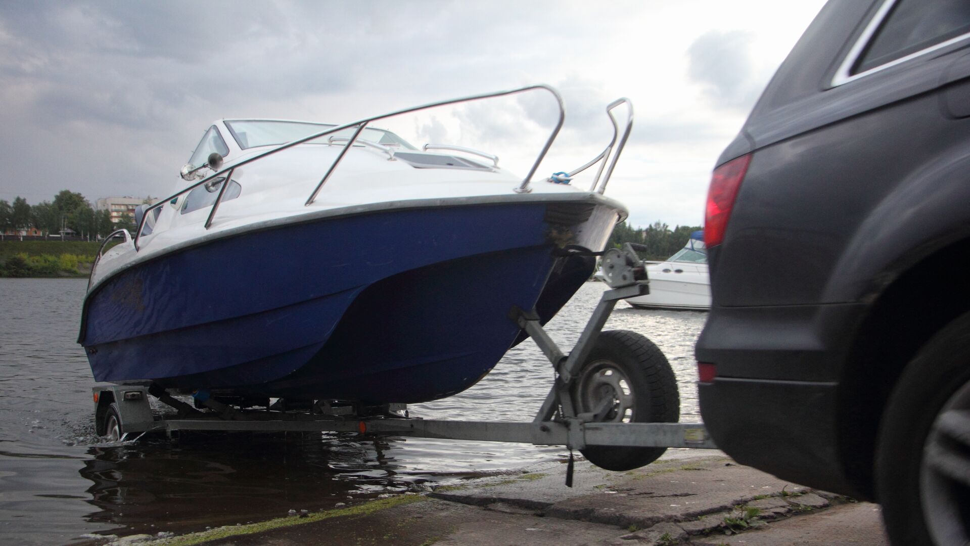 An SUV backs a boat on a trailer into the water for launch. 