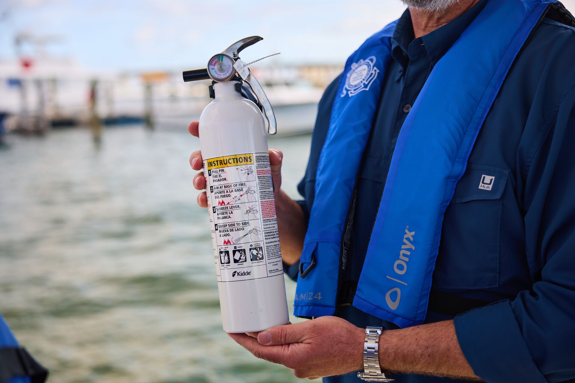 A boater wears a life jacket and holds a boat fire extinguisher.